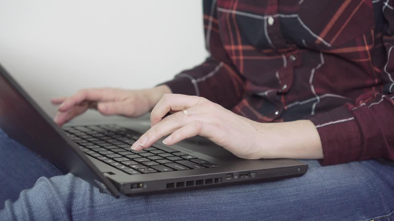 manos de una joven escribiendo en el teclado de una laptop negra - oficina en casa, toma lateral, primer plano