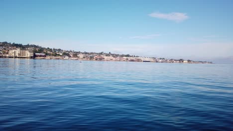 Gimbal-wide-shot-of-Cannery-Row-from-a-moving-boat-on-the-ocean-off-the-coast-of-Monterey,-California