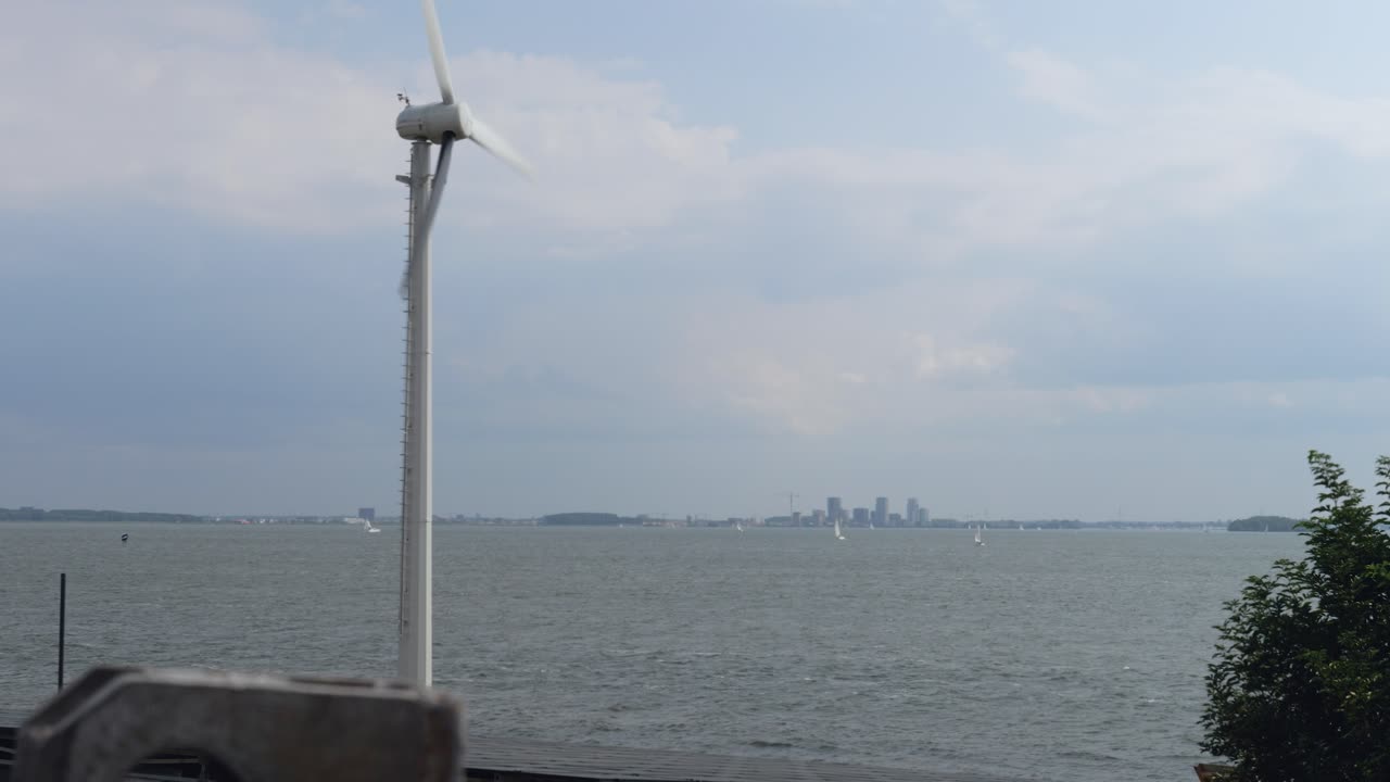 바다의 배경과 멀리 있는 도시의 실루을 배경으로 빠르게 회전하는 풍력 터빈