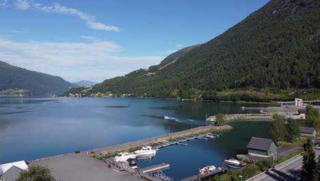 Ascending-aerial-close-to-three-Norway-flags-before-revealing-the-Innvikfjord-with-a-small-boat-sailing-out-from-the-marina---Loen-Norway