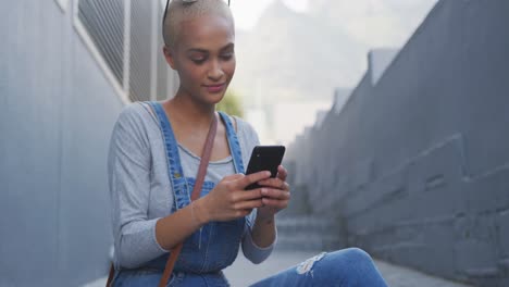 Frau-Mit-Gemischter-Abstammung-Sitzt-Mit-Smartphone-Auf-Einer-Außentreppe