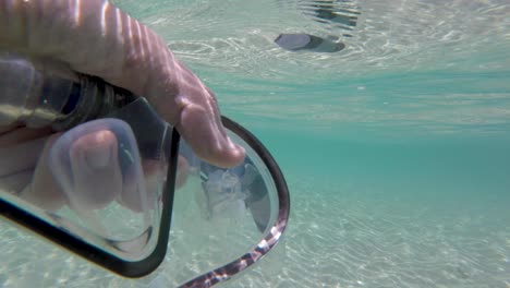 Underwater-walking-through-crystal-clear-ocean-water-in-paradise-on-remote-tropical-island-holding-dive-mask-and-snorkel-on-relaxing-pacific-holiday