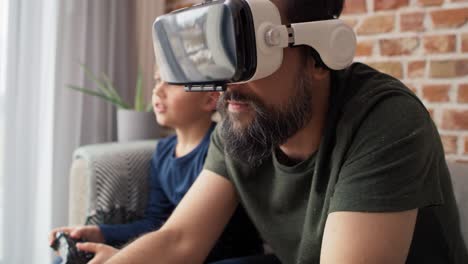 Video-Eines-Vaters,-Der-Eine-VR-Brille-Trägt-Und-Zu-Hause-Mit-Seinem-Sohn-Spielt.