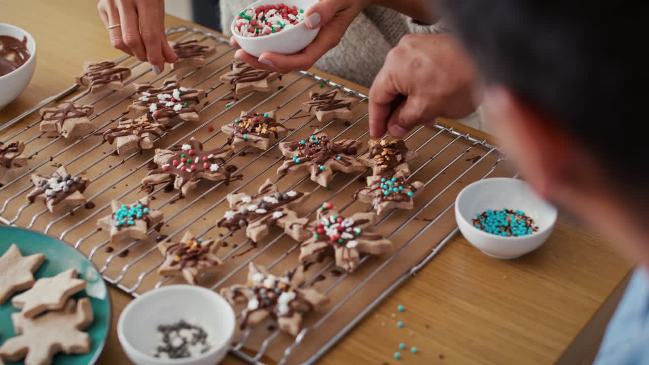 vista de alto ángulo de una pareja multiétnica decorando galletas dulces con salpicaduras coloridas durante la navidad.