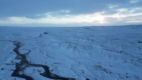 Snowy-sunrise-over-a-stream-in-the-north-of-Iceland-in-the-mountains,-aerial