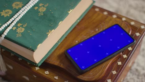 copia del corán en el stand en casa con cuentas de oración con teléfono móvil de pantalla azul