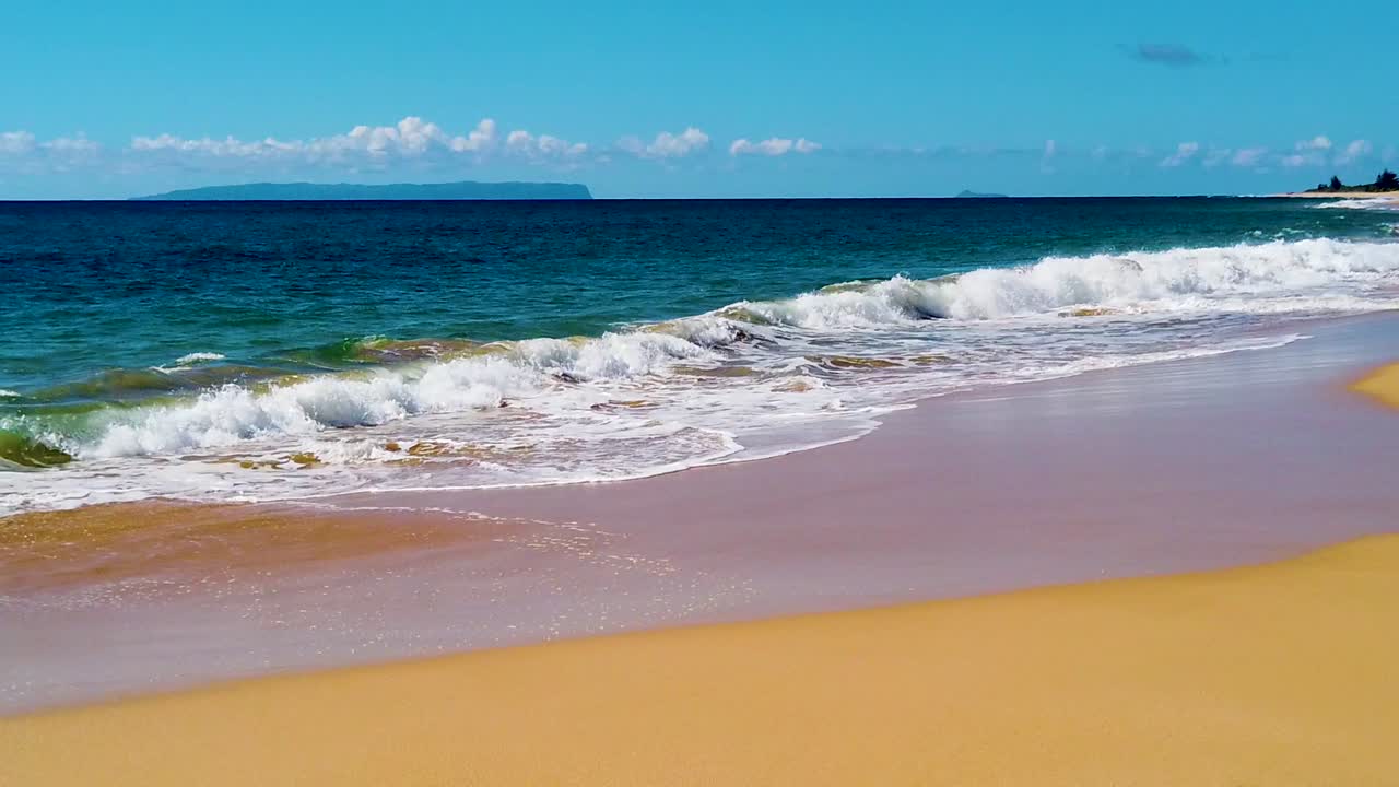 hd hawaii kauai cámara lenta panorámica de derecha a izquierda desde la playa a lo largo del marco inferior y derecho más allá de una isla en la distancia a las olas del océano rompiendo de borde a borde en el centro del marco con cielo mayormente soleado