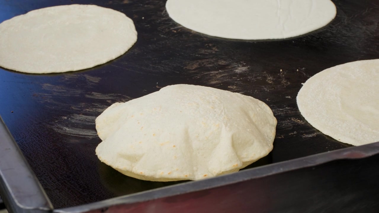 Traditional cooking footage showing inflated freshly made tortilla on flat grill during preparation of fresh handmade corn tortillas