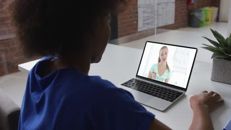 Back-view-of-african-american-woman-having-a-video-call-on-laptop-with-female-colleague-at-office