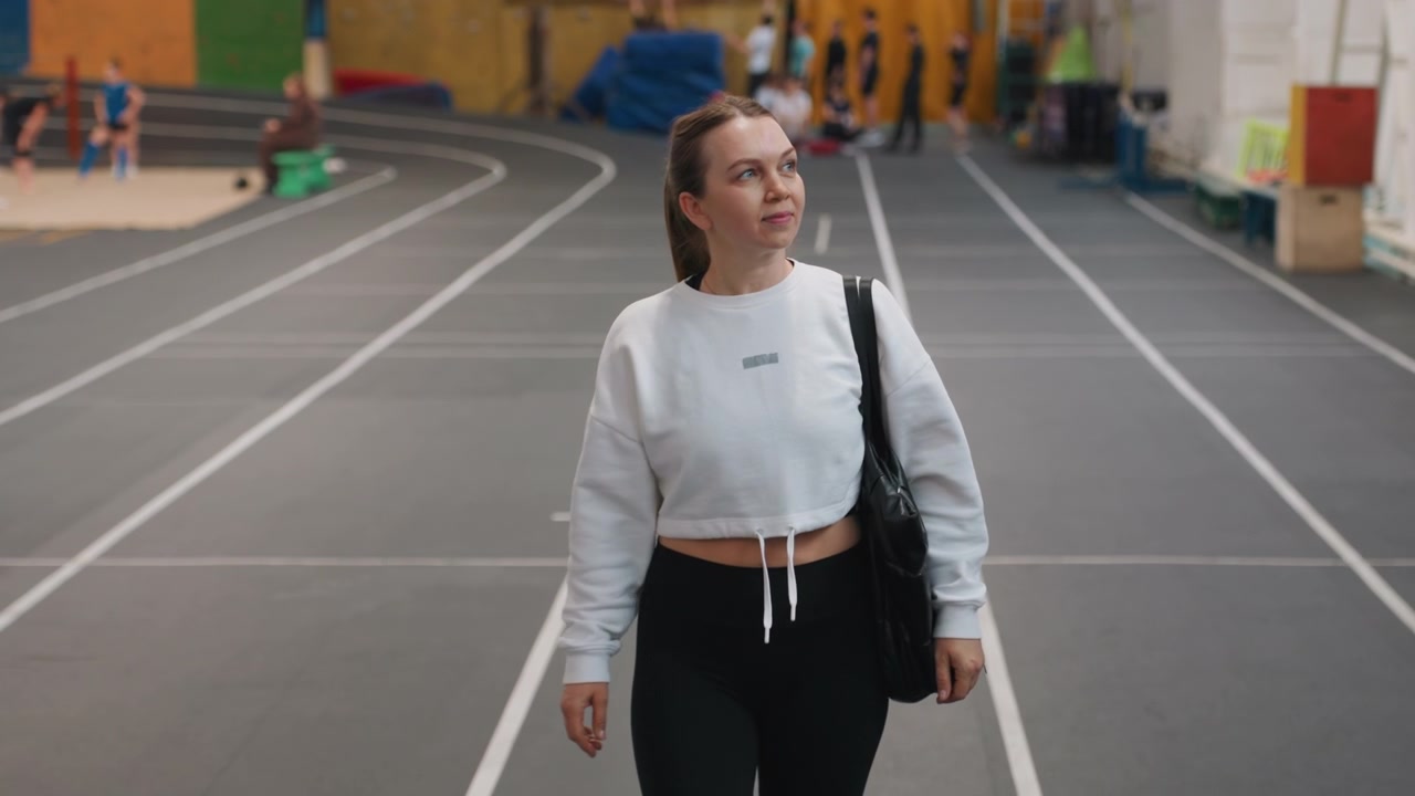 Spieler geht mit Trainertasche. Weibliche Athletin bewegt sich über den Badmintonplatz und beobachtet andere. Frau trägt Trainertasche und geht stetig über die Indoor-Badmintonfelder während einer Trainingseinheit.