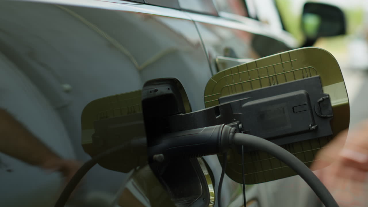 Sürücünün elektrikli aracın şarj portu kapağını açıp elektrik kablosunu takmasının yakın çekimi.