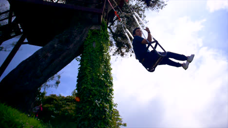 Young-man-goes-forward-on-rope-swing-in-Ecuador-nature,-side-slo-mo