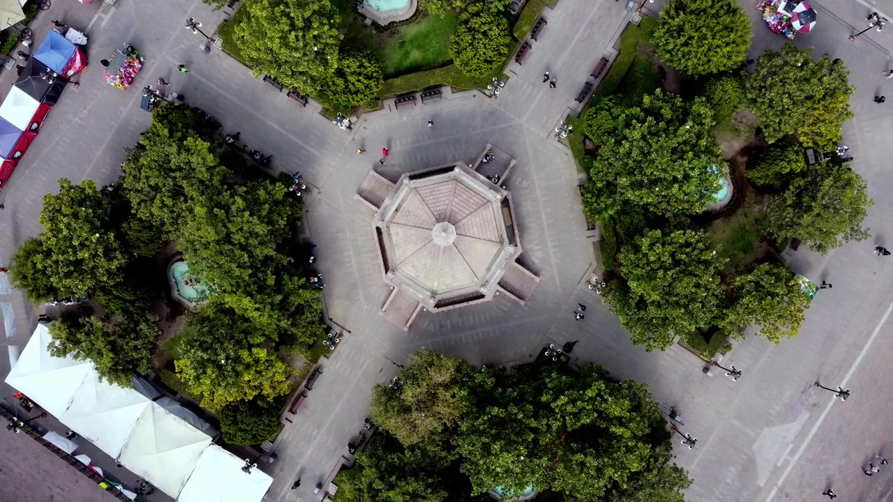 Top down aerial drone view of symmetrical town square featuring central pavilion pathways trees fountains and urban public space design
