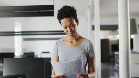 mujer de negocios biracial centrada comprobando documentos en la oficina