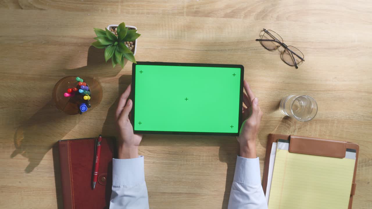 vista de arriba hacia abajo de una computadora portátil con pantalla verde simulada pantalla chromakey en un escritorio de oficina de madera al lado de la libreta con bolígrafos, gafas y un vaso de agua.