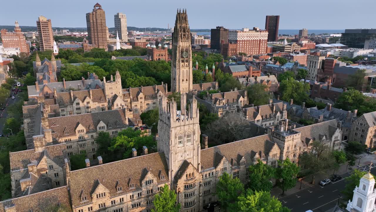 Harkness Tower at Yale old campus university of New Haven. American City in Connecticut at sunrise. Summer day with green trees. Connecticut Financial Center In background. Aerial approaching shot