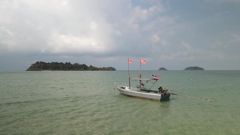 small boat with thai flag in tropical ocean with islands behind in windy weather