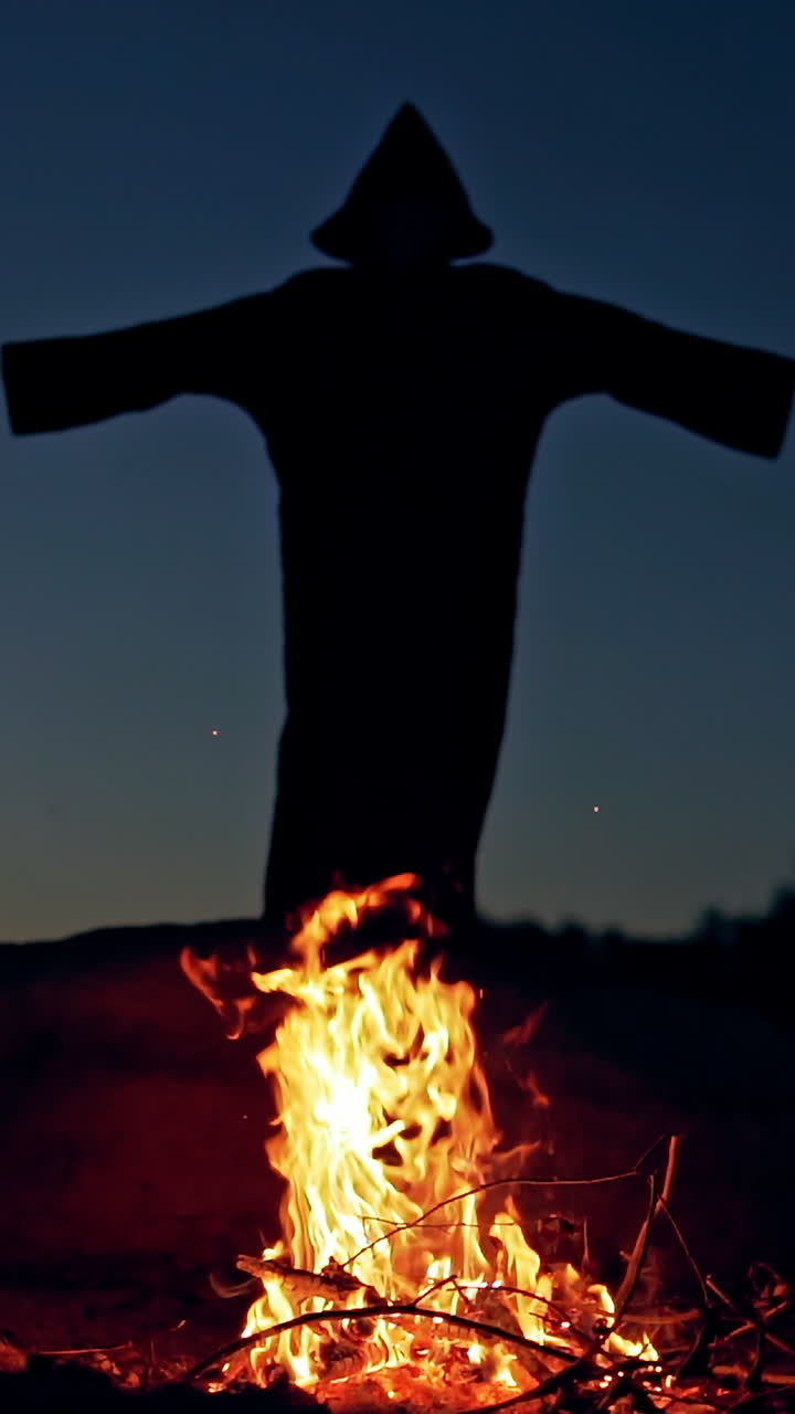 Black death behind the fire flame outdoors. Scary witch in black costume waving arms making fear on the background of burning fire. Halloween costume. Vertical video