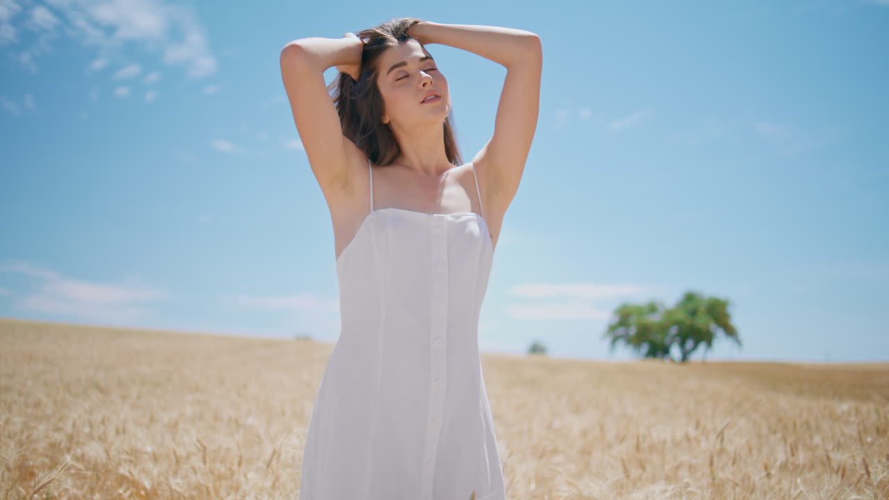Serene model warming sun at golden spikelets field horizon. Sensual girl posing