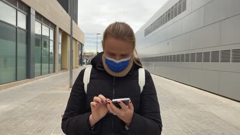 woman in mask walking to work and chatting online on smartphone