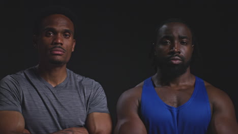 retrato de estudio de dos atletas masculinos entrenando o haciendo ejercicio en el gimnasio doblando los brazos contra un fondo negro