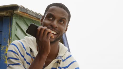 Vorderansicht-Eines-Jungen-Schwarzen-Mannes,-Der-An-Einem-Sonnigen-Tag-Am-Strand-Mit-Dem-Mobiltelefon-Spricht,-4K