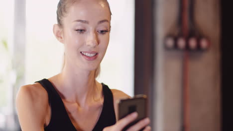 Beautiful-Female-Athlete-Using-Mobile-Phone-During-Break-After-Workout-At-Fitness-Club