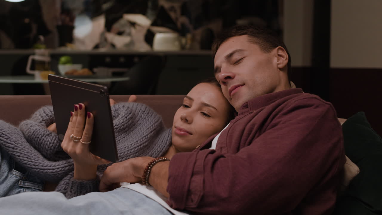 пара отдыхает на диване, смотрит планшет.