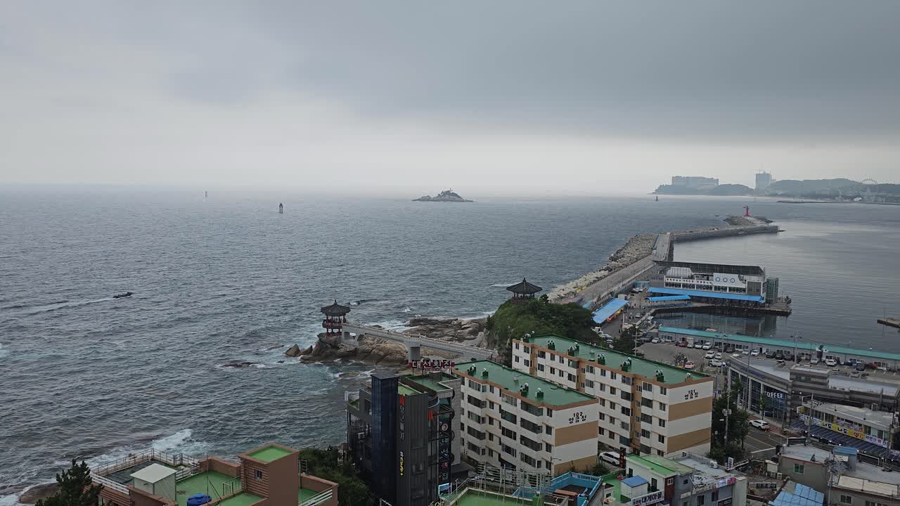 Ocean Wave Crashing On The Rocky Coastline With Yeonggeumjeong Pavilion Seen From Sokcho Lighthouse On A Rainy Day
