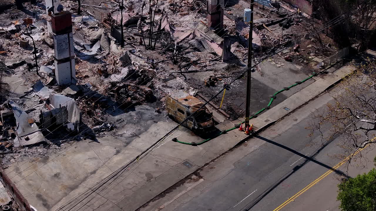 Aerial view of an urban area devastated by fire, showing burnt buildings and a charred vehicle