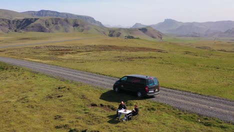 aerial over two men enjoying a picnic beside a black camper van in the mountains of iceland