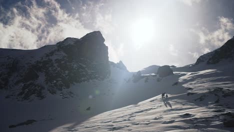 off-piste skiers walks up a huge mountain with their skis on the back