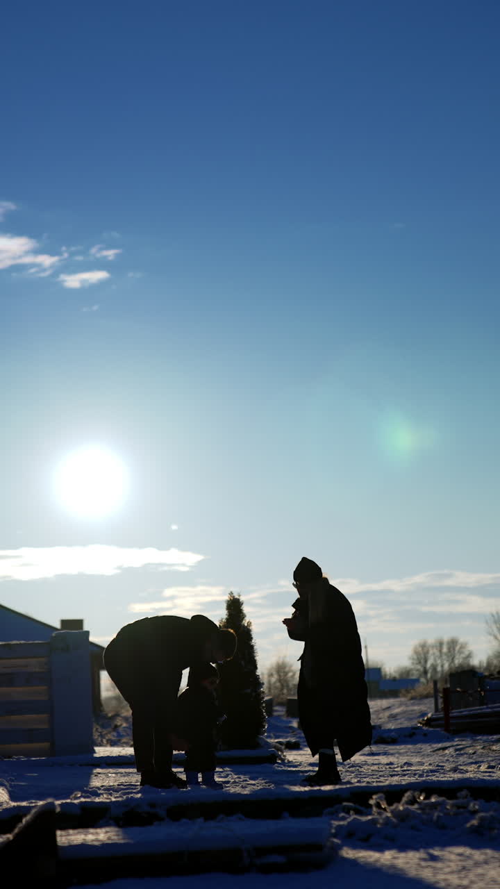 Silhouettes of man, woman and baby wearing warm clothes in winter. Father tosses a kid high up playing with him. Vertical video.
