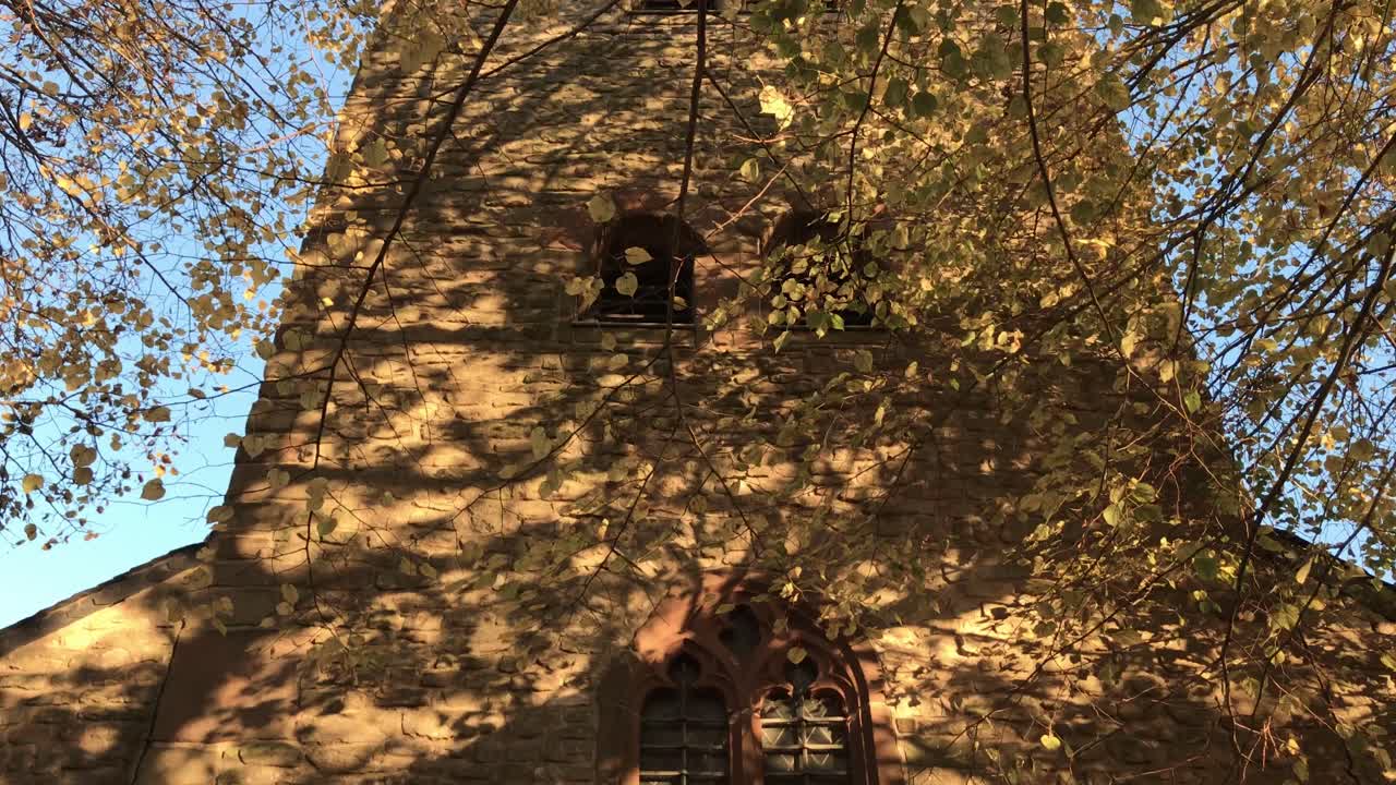 Pan up to down of church tower, Autumn with leaves falling. Blue sky. Girsterklaus in Luxembourg.