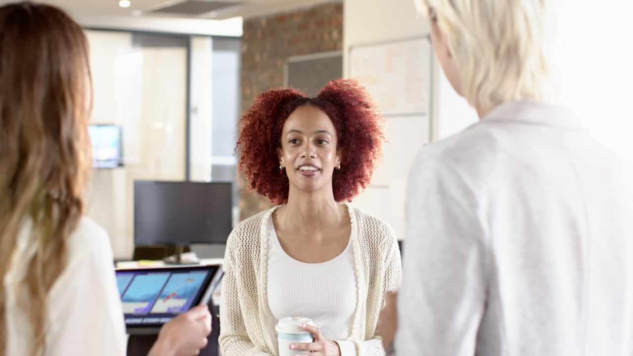Discussing project, woman holding coffee cup while colleagues use tablet in office