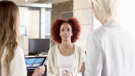 discussing project, woman holding coffee cup while colleagues use tablet in office