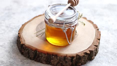 glass jar full of fresh honey placed on slice of wood