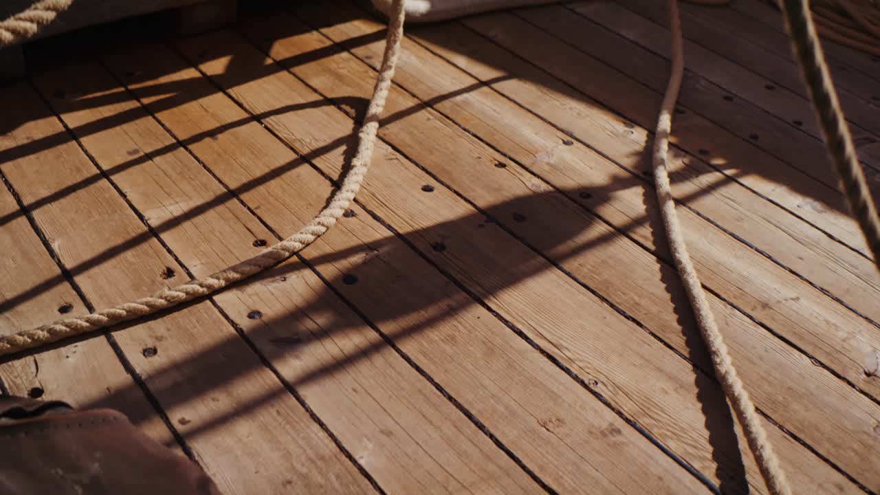 Close-up of sailing ropes and shadows on wooden deck, warm sunlight creating patterns across planks, nautical detail and maritime atmosphere concept