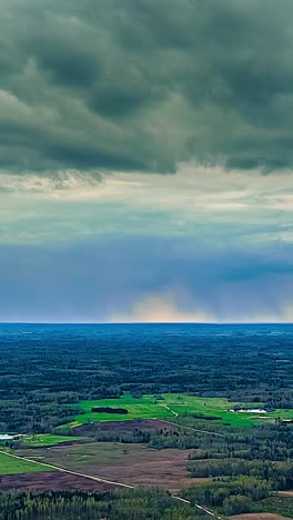 an aerial timelapse captures dark, dramatic storm clouds gathering and moving ominously across the sky above a vast forest and green fields in the remote latvian countryside.