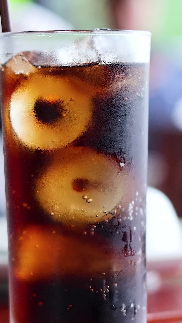 Un bicchiere alto di cola fredda con cubetti di ghiaccio e condensa in un'inquadratura verticale.