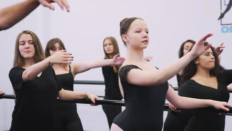 female students at performing arts school rehearsing ballet in dance studio using barre