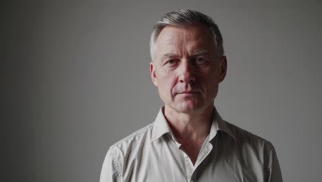 un hombre de negocios profesional de mediana edad manteniendo un comportamiento tranquilo, proyectando una tranquila confianza a través de una expresión neutral y contacto visual directo contra un fondo de estudio gris sin costuras.