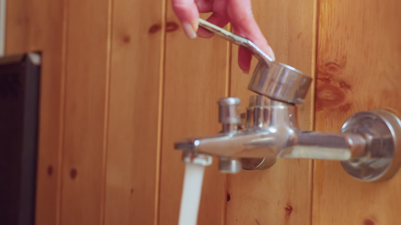 close up of person hand gently turning on sauna bathroom chrome tap to pour water into basin, polished nail detail and wood panel background conveying tactile moment of control and refreshment
