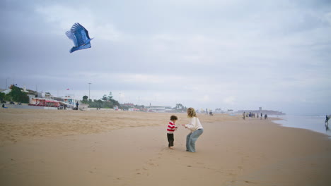 little son playing kite with parent on beach. joyful mother helping teach child