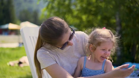 Closeup-Mom-and-daughter-are-sitting-on-beach-near-the-bushes