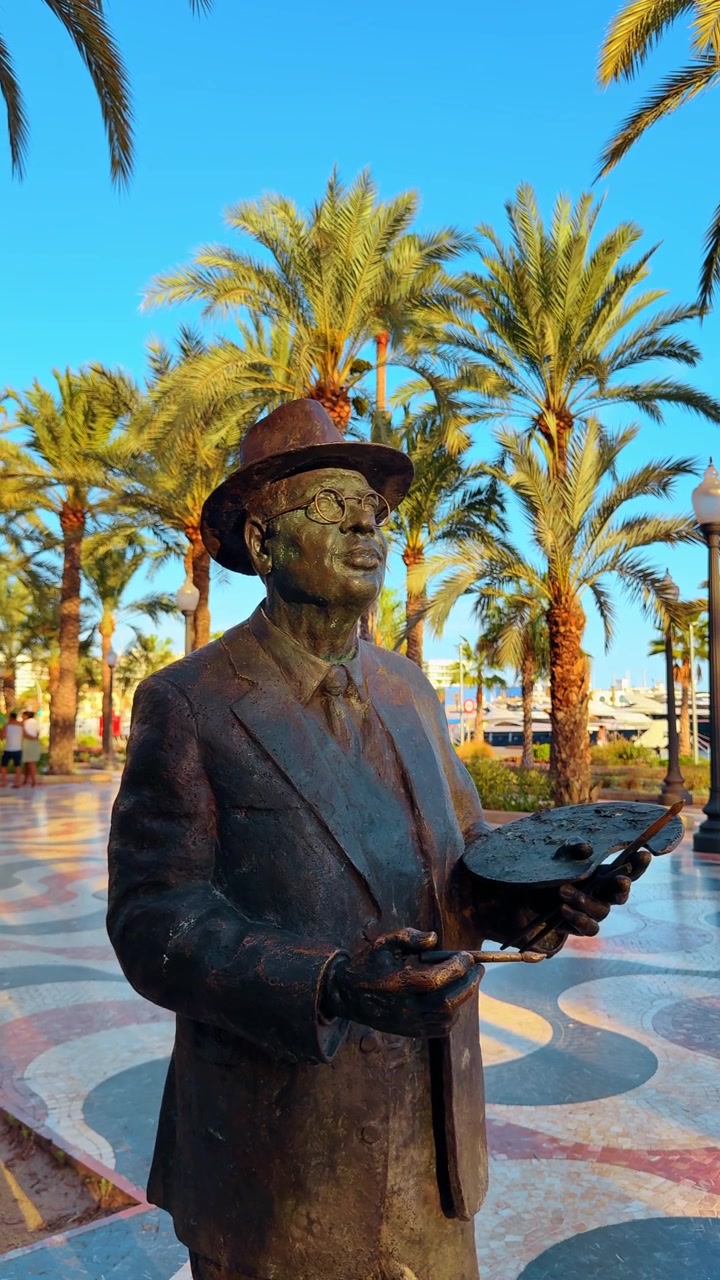 Madrid, Spagna, 8 agosto 2025: Statua del pittore Gaston Castello sul lungomare di Alicante. Monumento in bronzo di un artista che tiene una tavolozza con palme e un lungomare sullo sfondo.