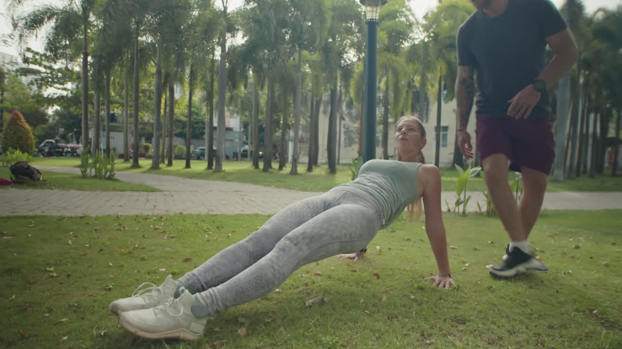 Woman Doing Reverse Plank with Help of Personal Trainer in Park