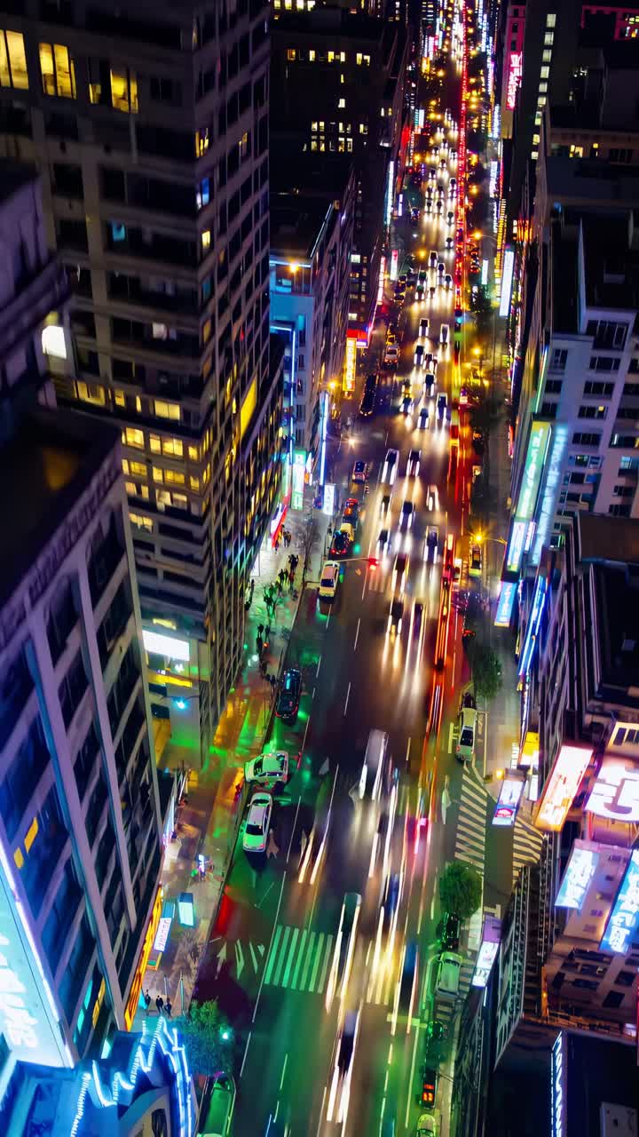 Aerial view of a bustling city street at night, with vibrant lights and blurred traffic