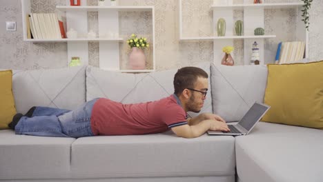 hombre enano acostado en el sofá en casa usando una computadora portátil.