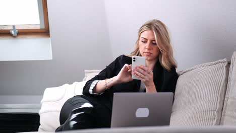 a young businesswoman sits on the sofa and surfs on her smartphone